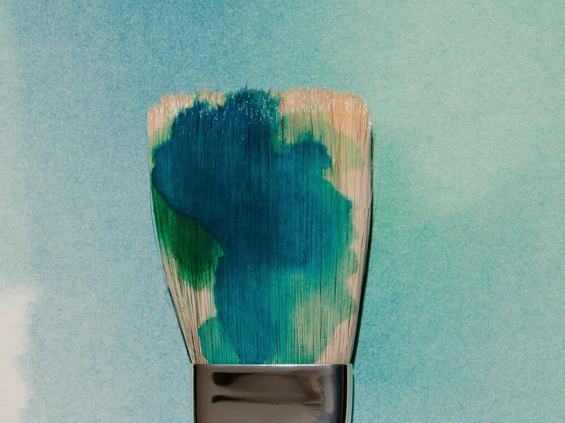 Pinselborsten mit blaugrüner Farbe berühren strukturiertes Aquarellpapier in Nahaufnahme